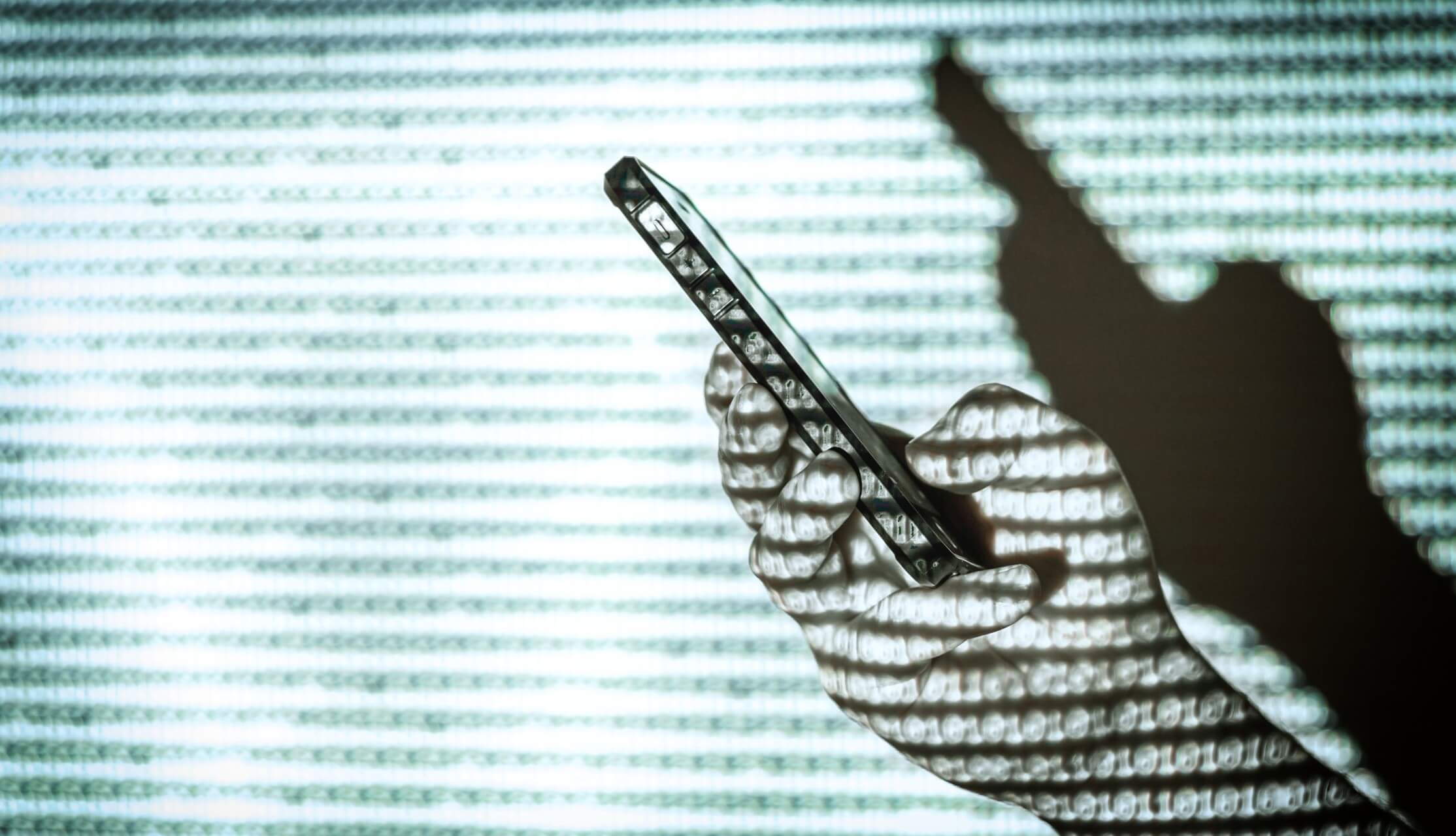 Pessoa com telemóvel na mão à frente de linhas de código e painel de segurança digital